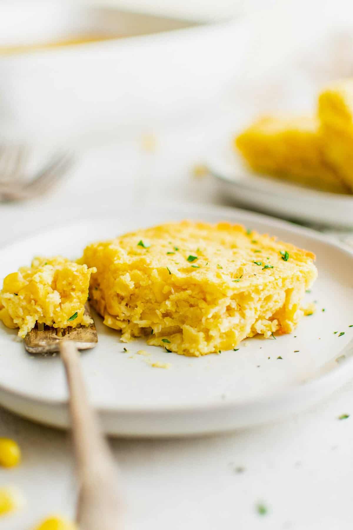 A slice of cornbread casserole on a plate with a bite taken out of it.