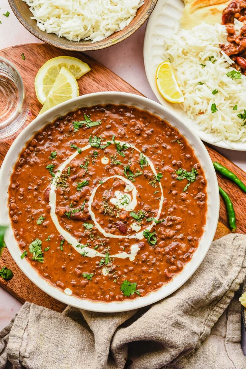 A bowl of dal makhani is presented on a wooden surface next to a beige linen tea cloth.