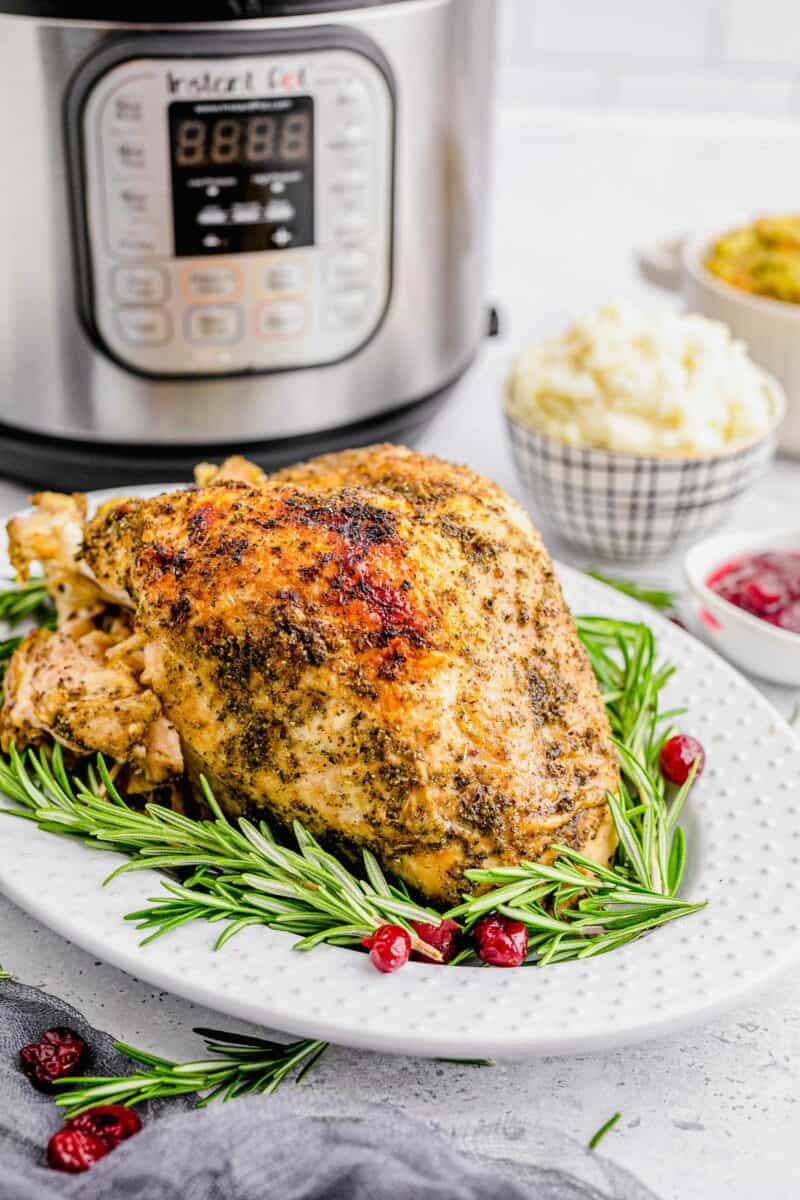 Turkey breast is presented on a white plate with rosemary sprigs and cranberries. 