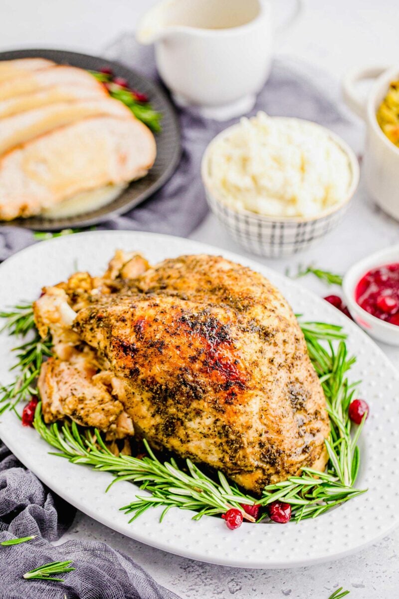 Fresh rosemary and candied cranberries are placed around a roasted turkey breast.