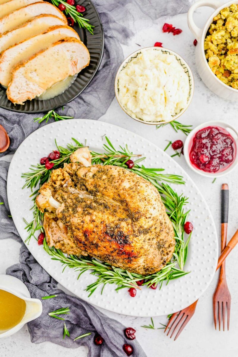 Roasted turkey is surrounded by cranberry sauce, mashed potatoes, stuffing, and flatwarre. 