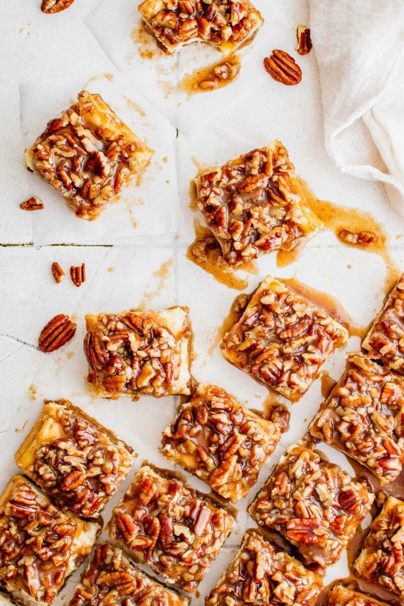 Several pecan pie cheesecake bars are sliced and presented on a white surface. 