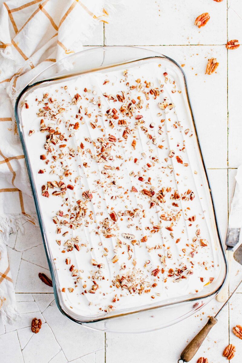 Crushed pecans are sprinkled across the top of whipped cream in a baking dish.