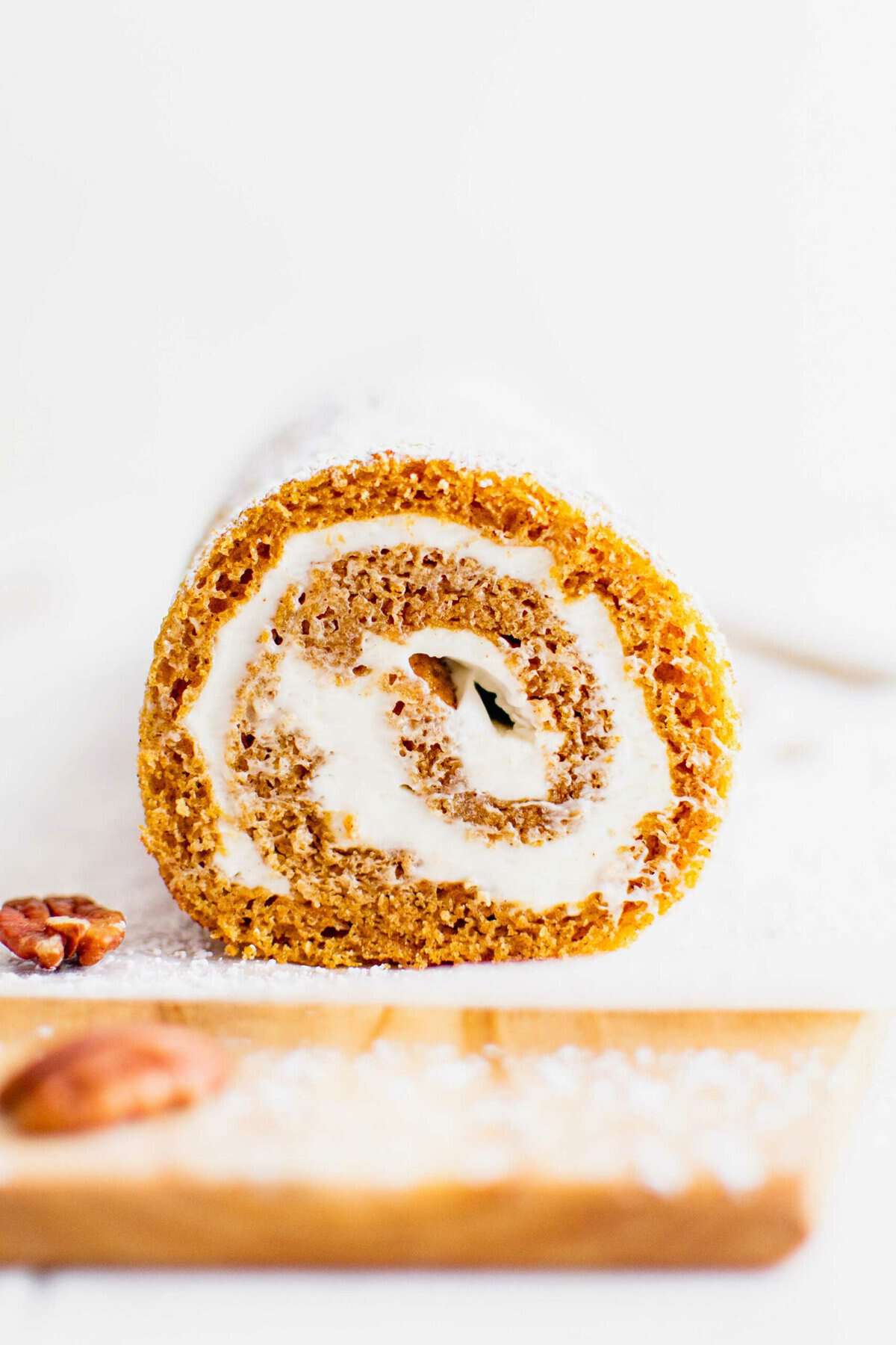 Front view of a pumpkin roll on a wooden cutting board lined with parchment paper.