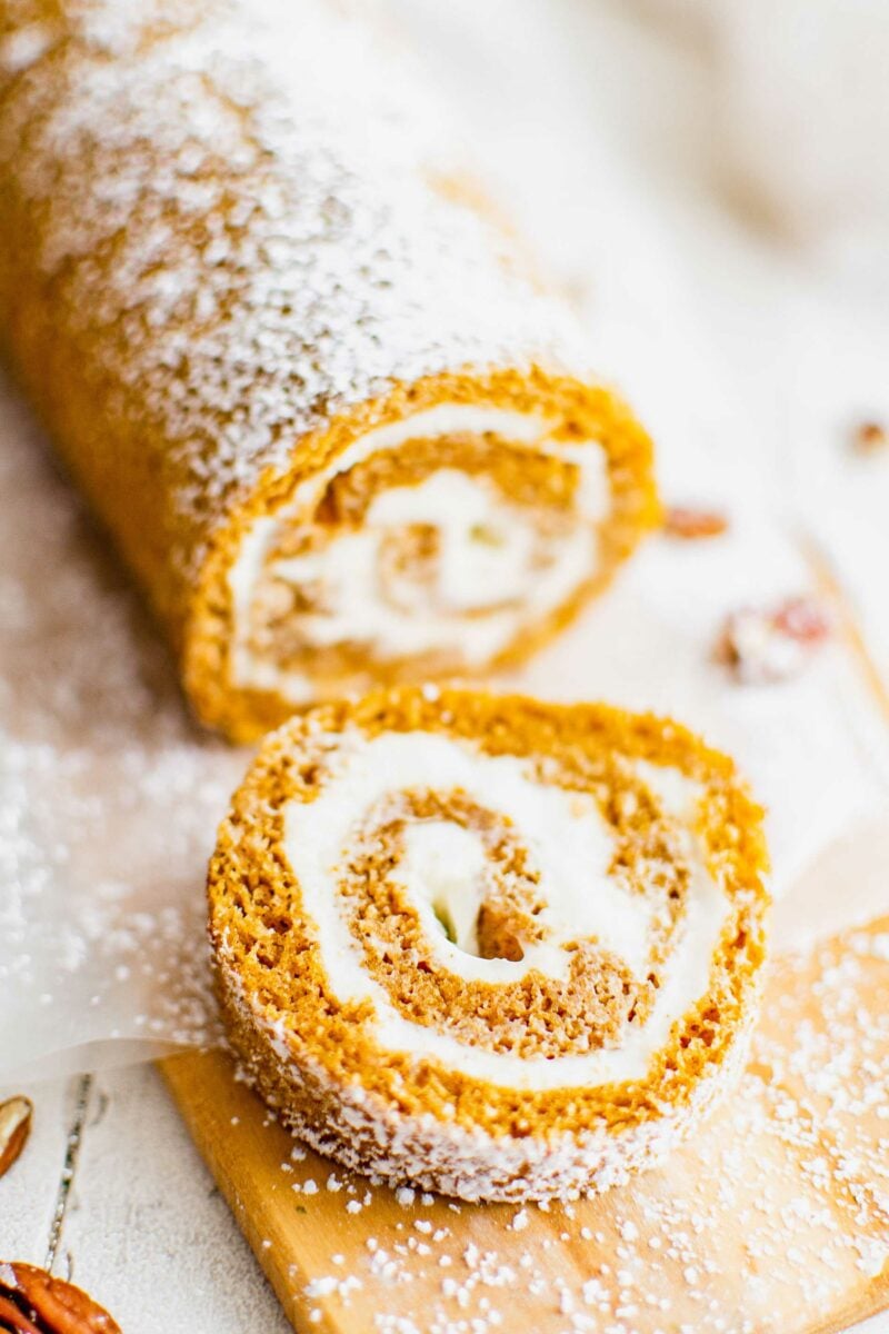 A swirled slice of pumpkin roll is presented on a powdered sugar coated surface. 
