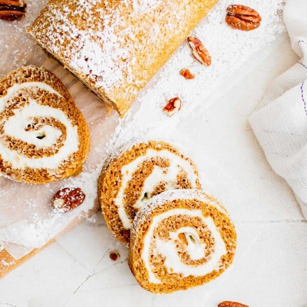 Overhead view of a pumpkin roll cut into slices on a white coutertop.