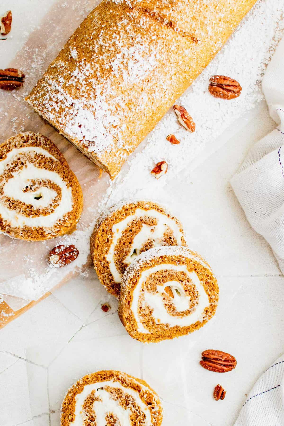 Overhead view of a pumpkin roll cut into slices on a white coutertop.