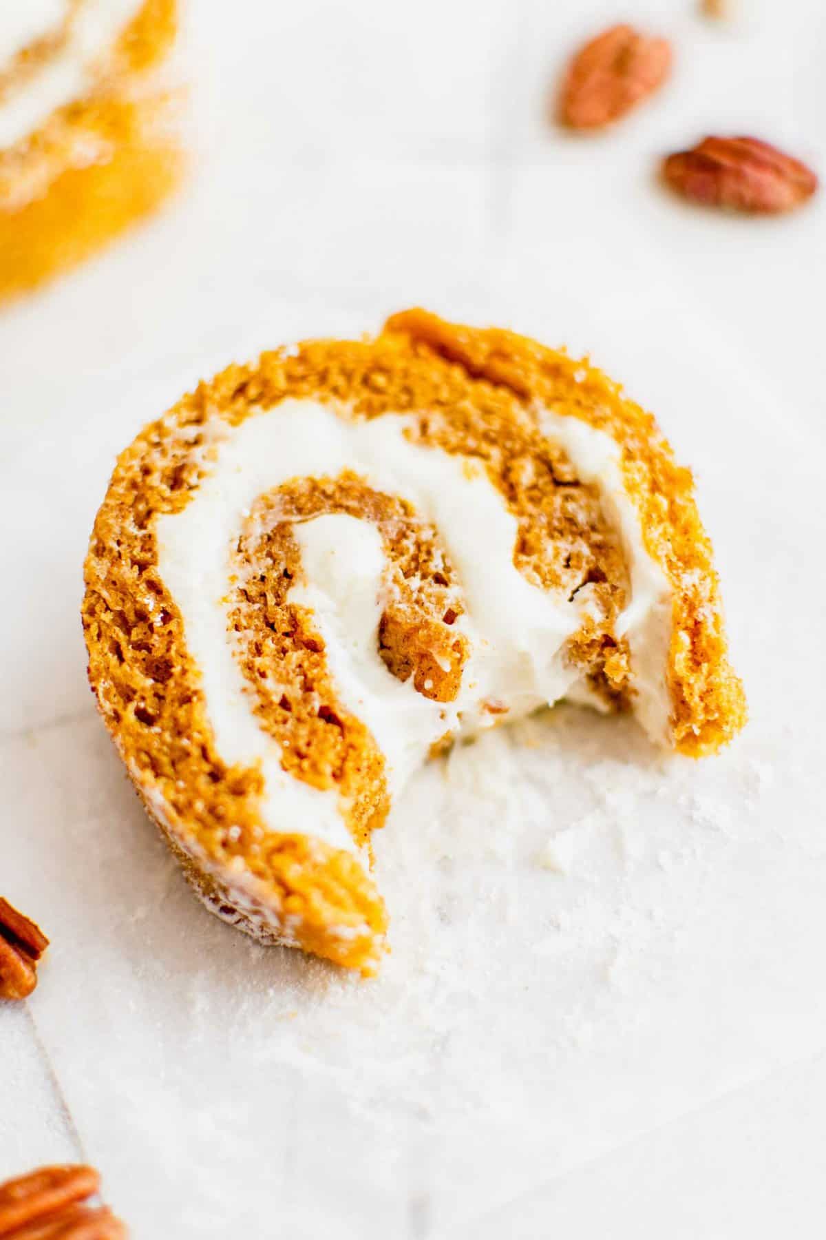 Overhead view of a pumpkin roll slice with a bite missing on a white countertop.