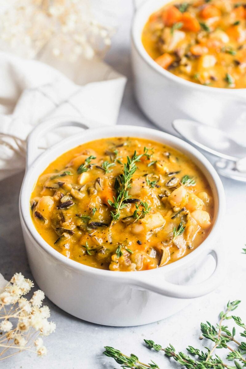 A white pot is filled to the brim with soup and is topped with fresh thyme. 