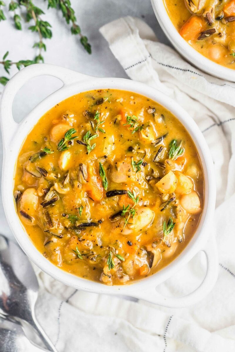 Fresh herbs garnish a full white bowl of pumpkin wild rice soup. 