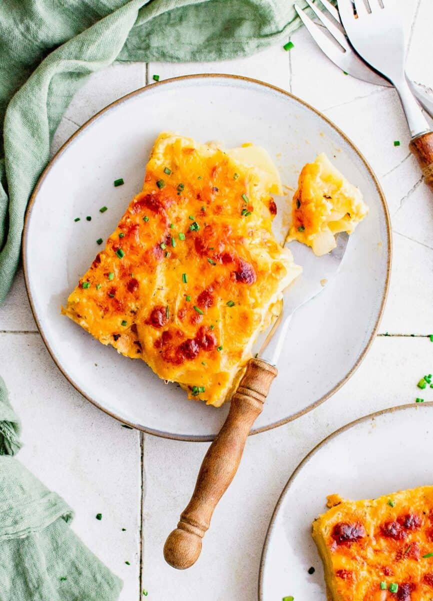 A fork is on a plate with a serving of scalloped potatoes. 