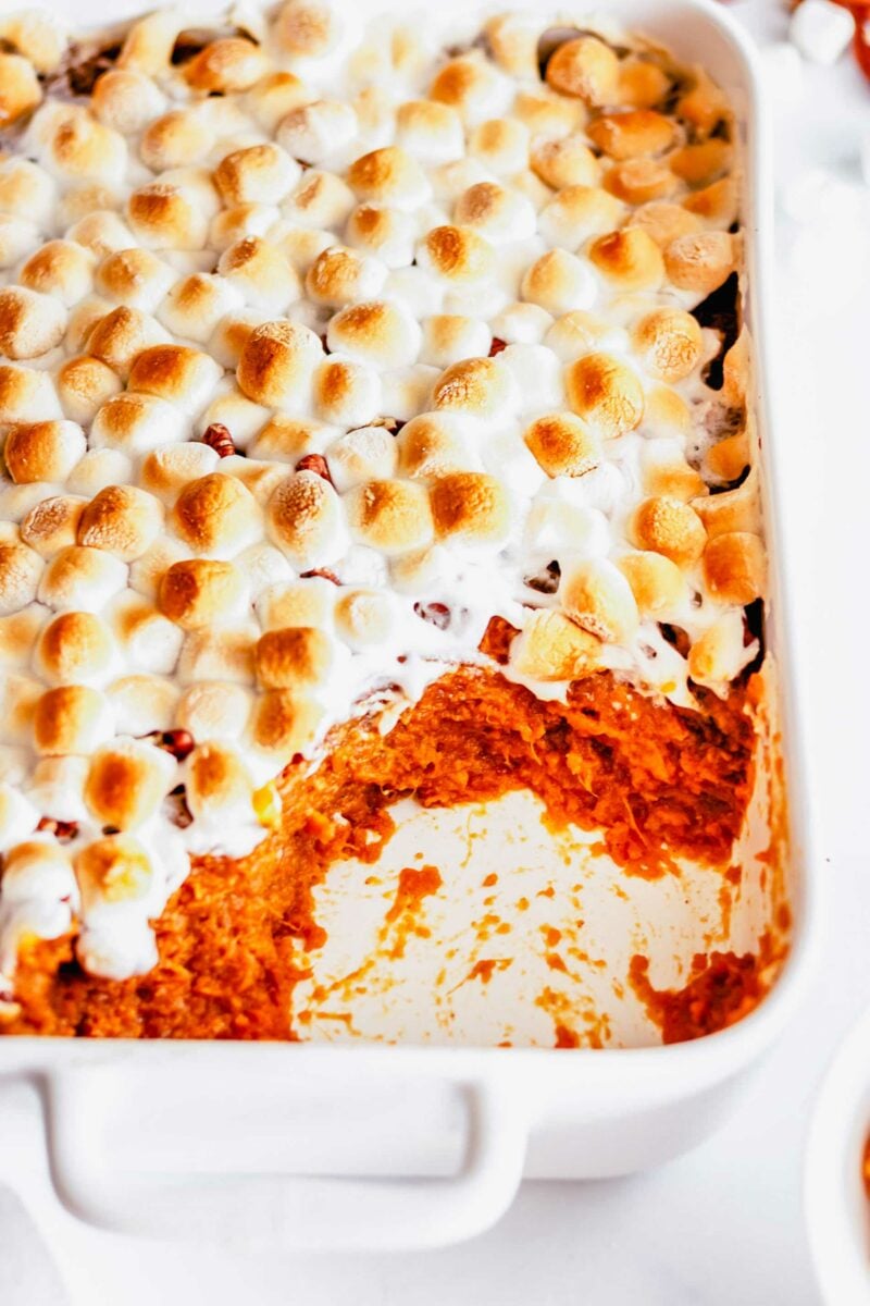 A portion of sweet potatoes has been removed from a white casserole dish.