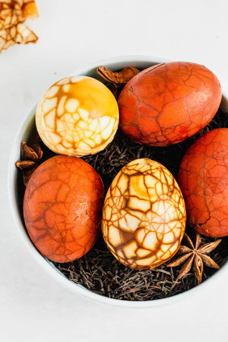 Overhead shot of marbled Taiwanese tea eggs on a bed of loose black tea in a white bowl