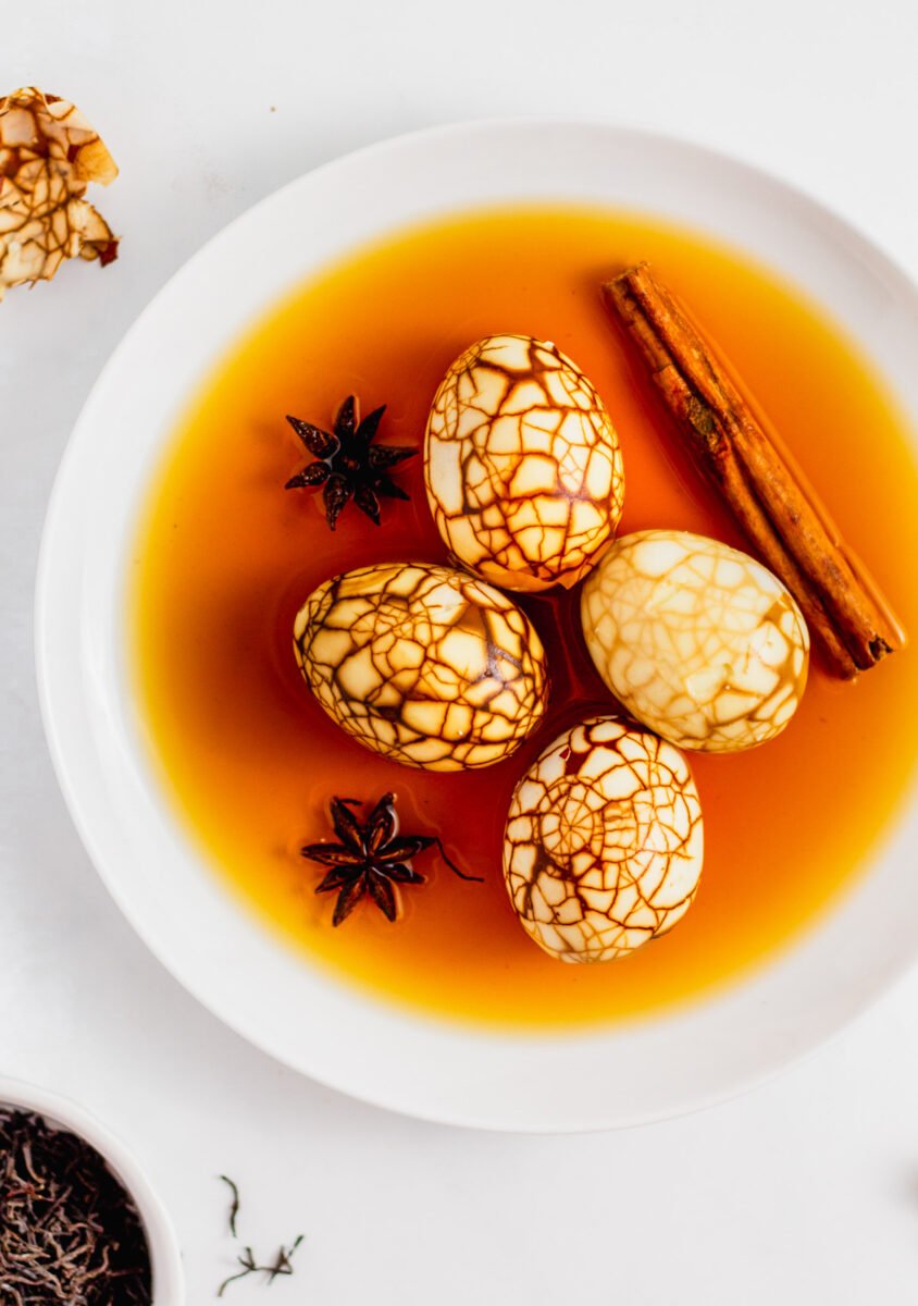 Overhead shot of marbled Taiwanese tea eggs all peeled on a white plate with braising liquid, star anise, and cinnamon stick.
