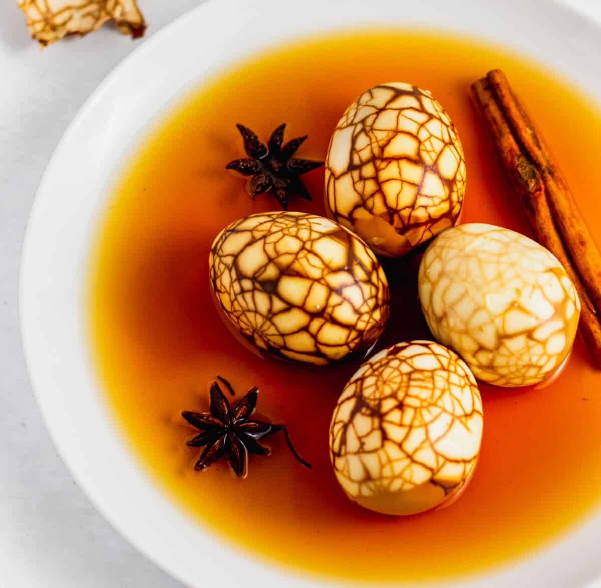 Up close shot of marbled Taiwanese tea eggs all peeled on a white plate with braising liquid, star anise, and cinnamon stick.