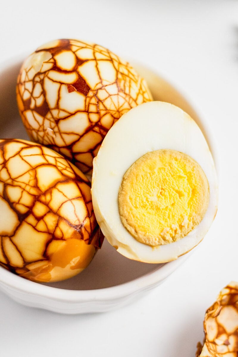 Halved Taiwanese tea eggs all peeled in a white bowl with cooked egg yolk exposed.