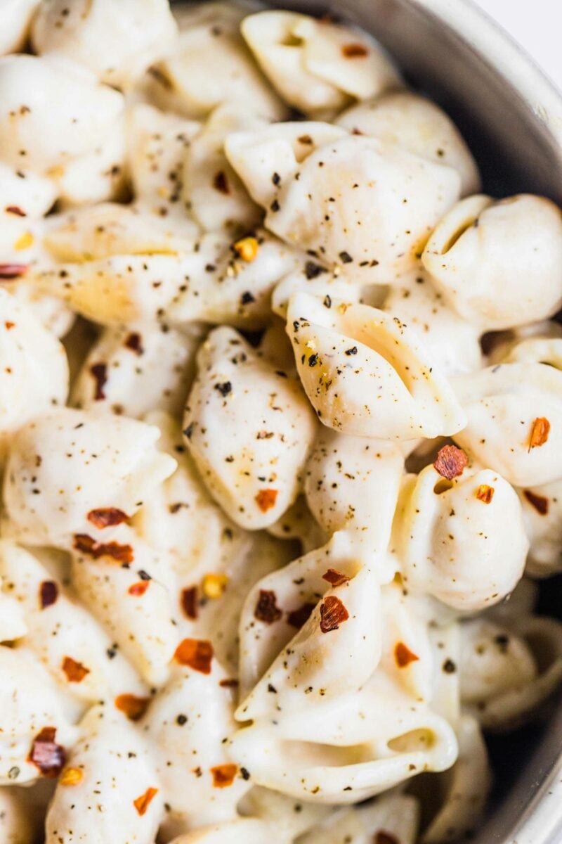 Red pepper flakes and black pepper are sprinkled on top of creamy pasta shells. 