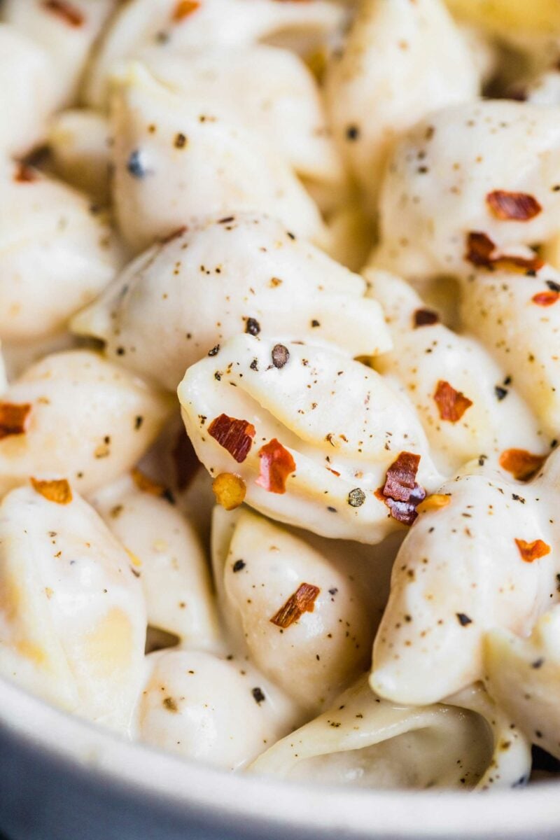 Red pepper flakes and cracked black pepper are sprinkled across a serving of creamy vegan pasta shells. 