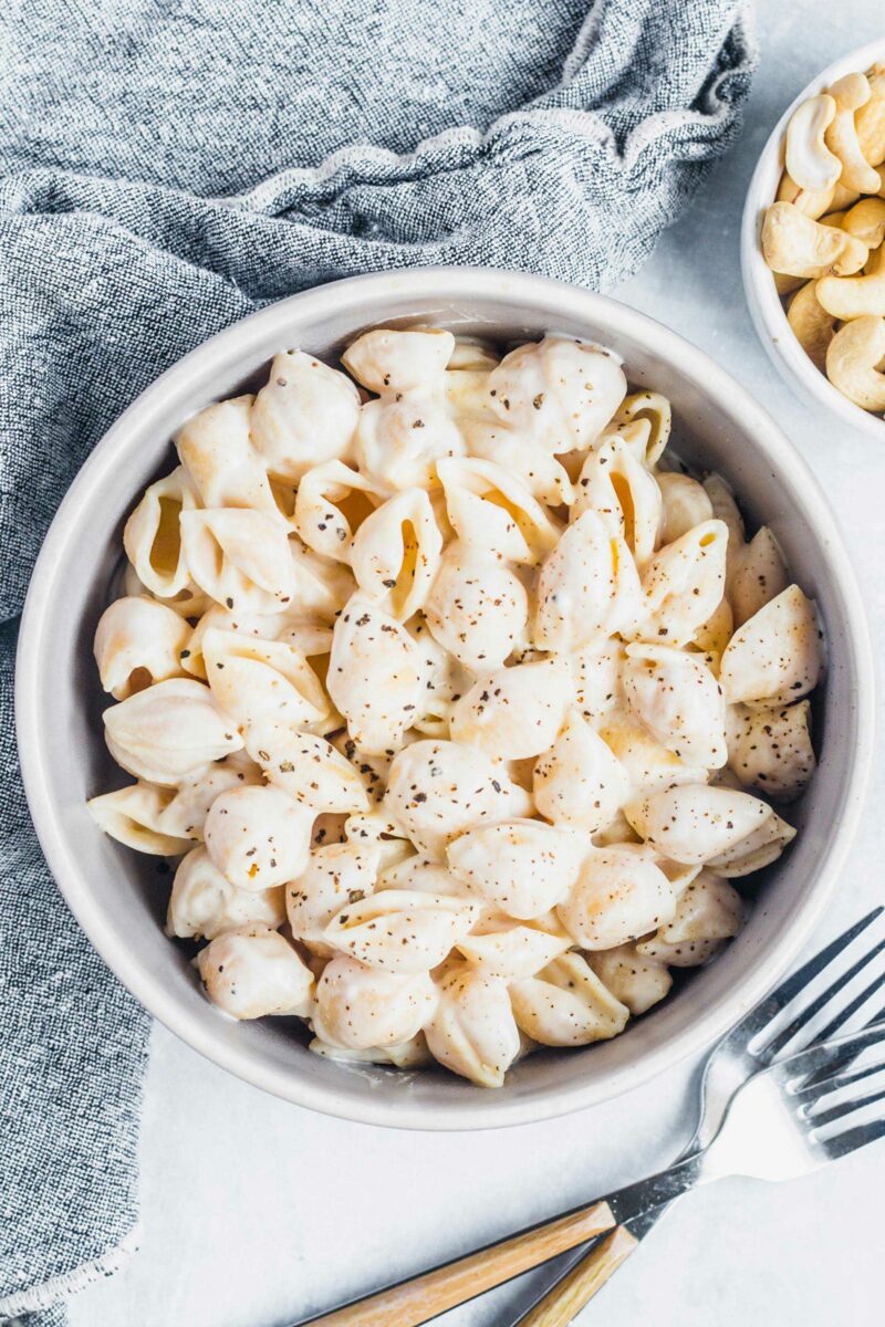 A bowl of creamy pasta shells are topped off with fresh cracked black pepper. 