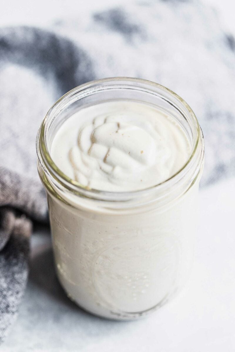 A glass mason jar is filled to the top with white sauce.