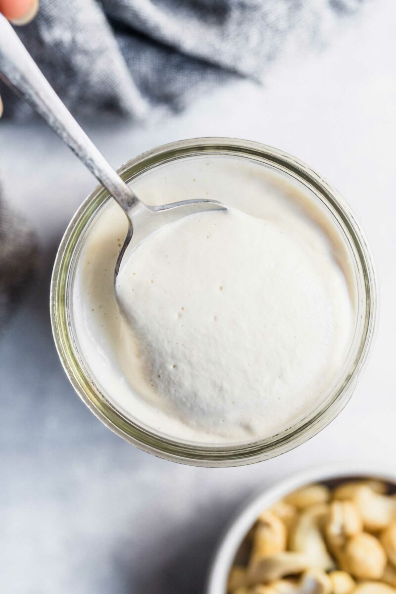 A spoon is dipped into a jar of vegan cream sauce.