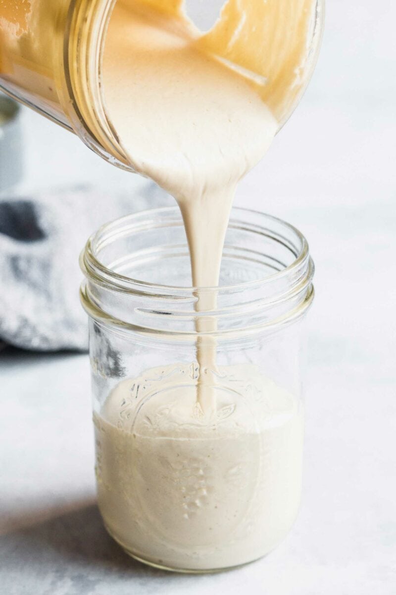 Cashew cream sauce is being poured into a jar. 