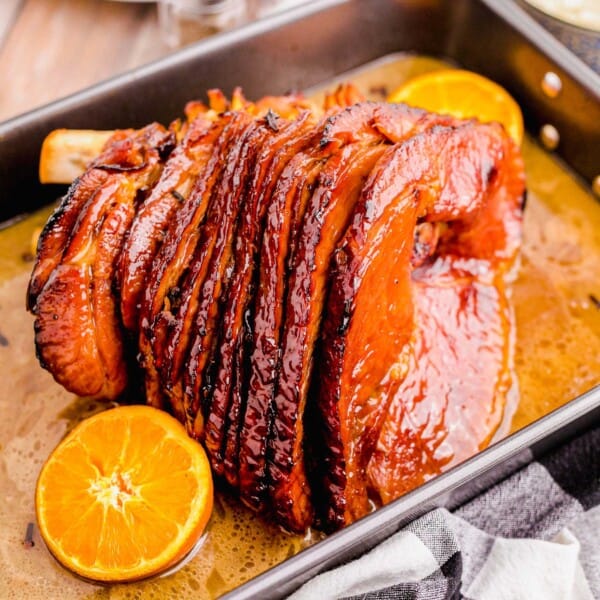 spiral baked glaze ham in a roasting pan with halved oranges and au jus