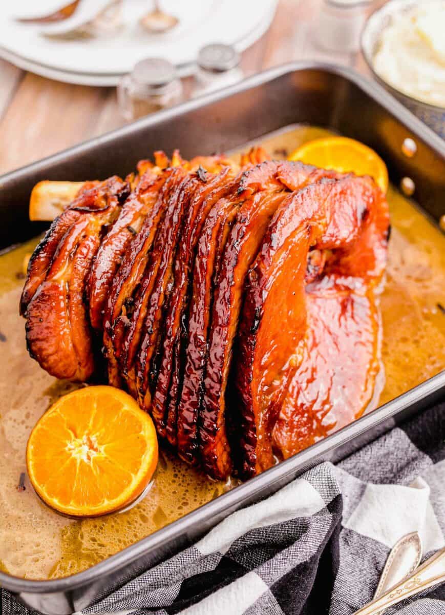 A spiral cut baked ham is presented in a tray with orange halves. 