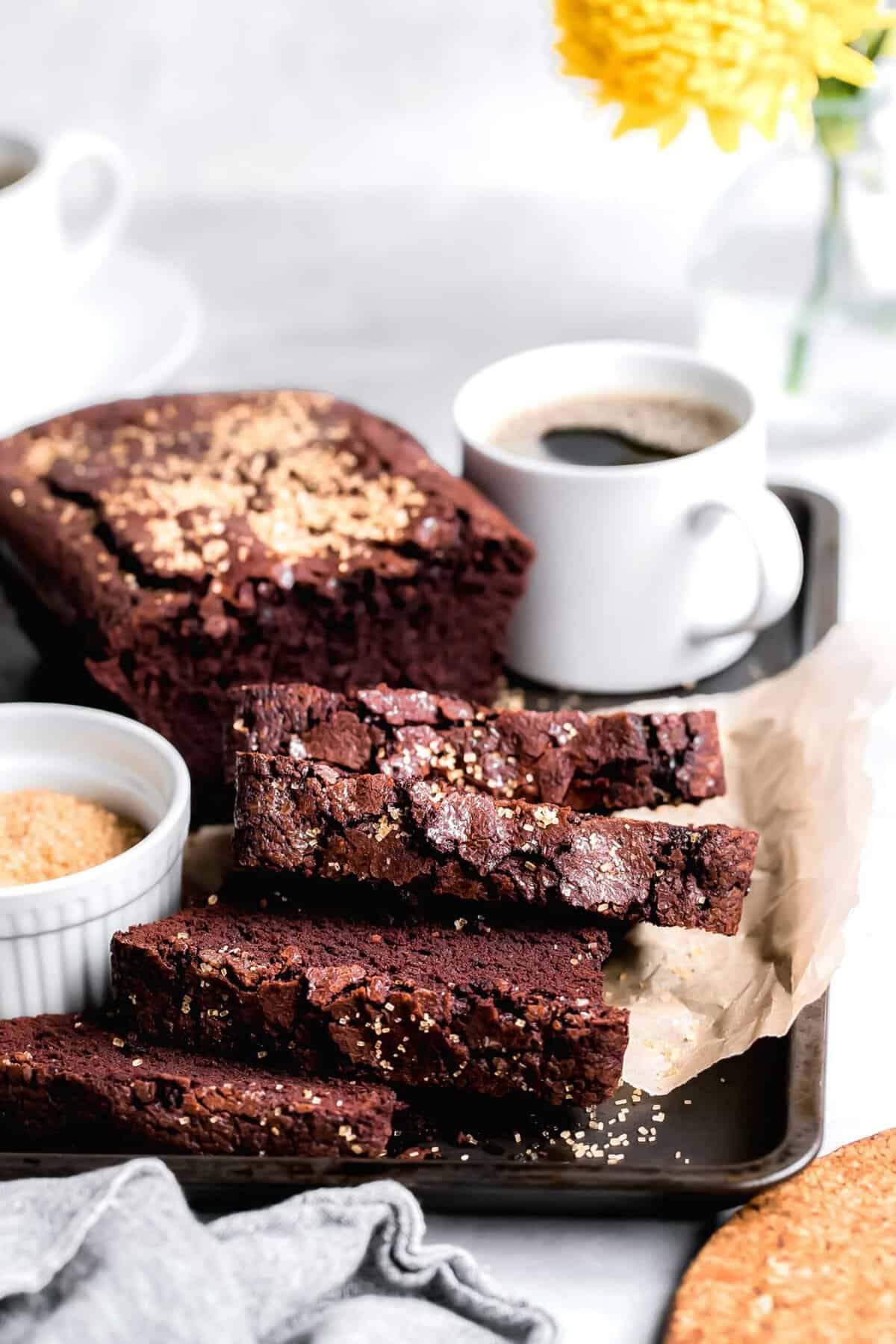 Slices of chocolate cinnamon bread on parchment-lined baking sheet with mug of coffee