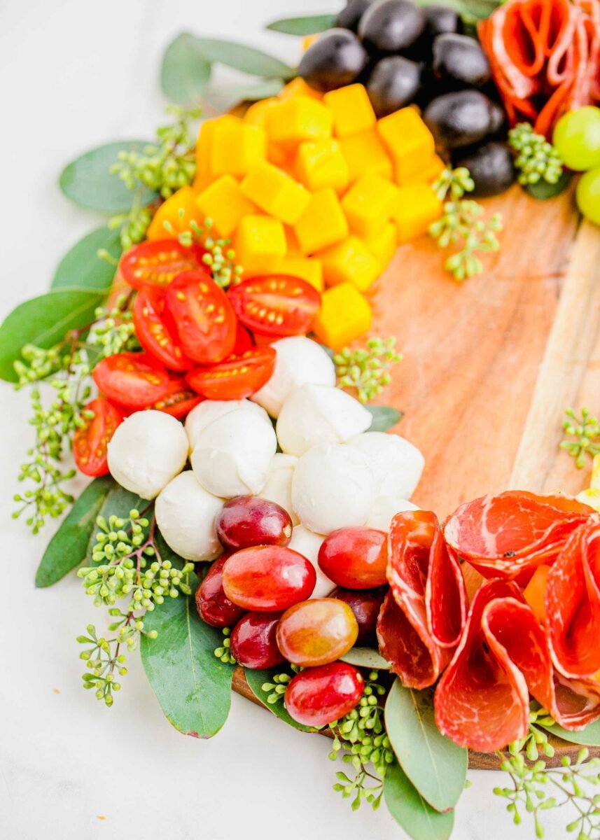 Grapes, salami, mozzarella balls, tomatoes and cheese are placed in a circle on a wooden cutting board. 