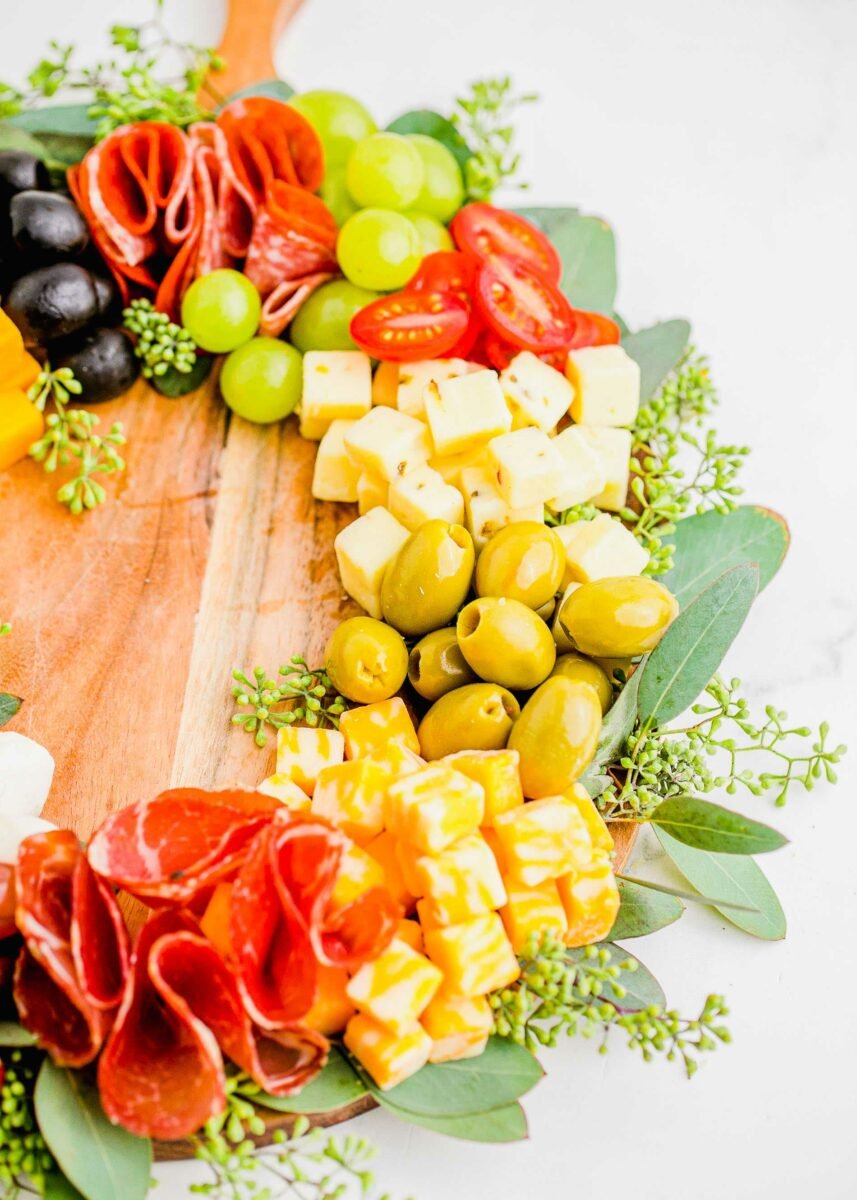 Salami, cheese, olives and more are presented in a circle on a wooden cutting board. 