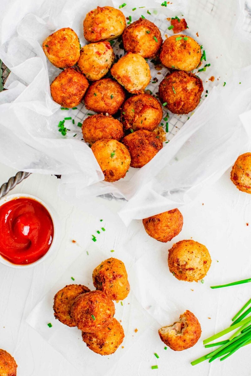 A basket is lined with parchment paper and filled with fried mashed potato balls.