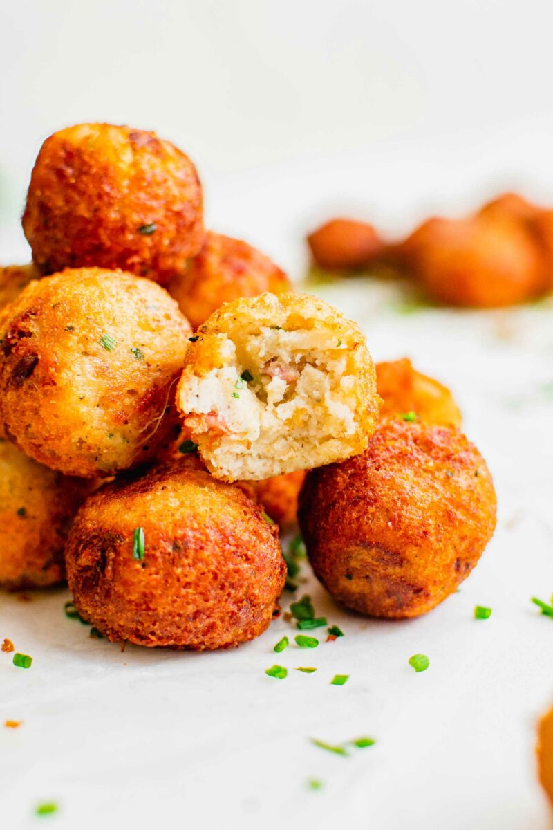 Chopped chives are sprinkled on top of a pile of mashed potato balls. 
