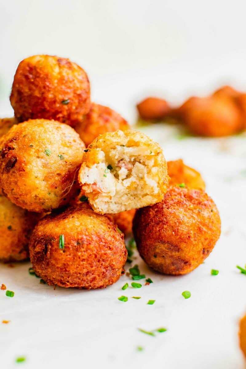 Chopped chives are sprinkled on top of a pile of mashed potato balls.