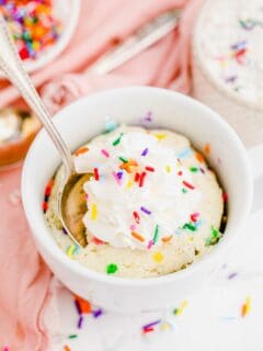 Spoon digging into funfetti mug cake topped with whipped cream and sprinkles