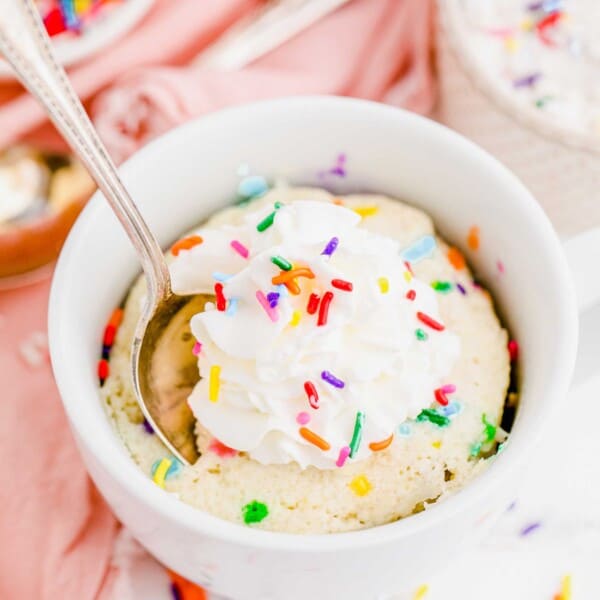 Spoon digging into funfetti mug cake topped with whipped cream and sprinkles