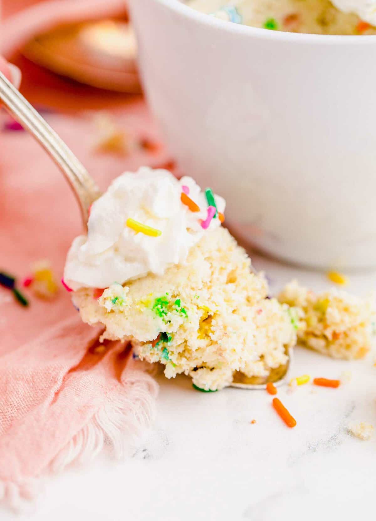 Spoonful of funfetti mug cake topped with whipped cream and sprinkles