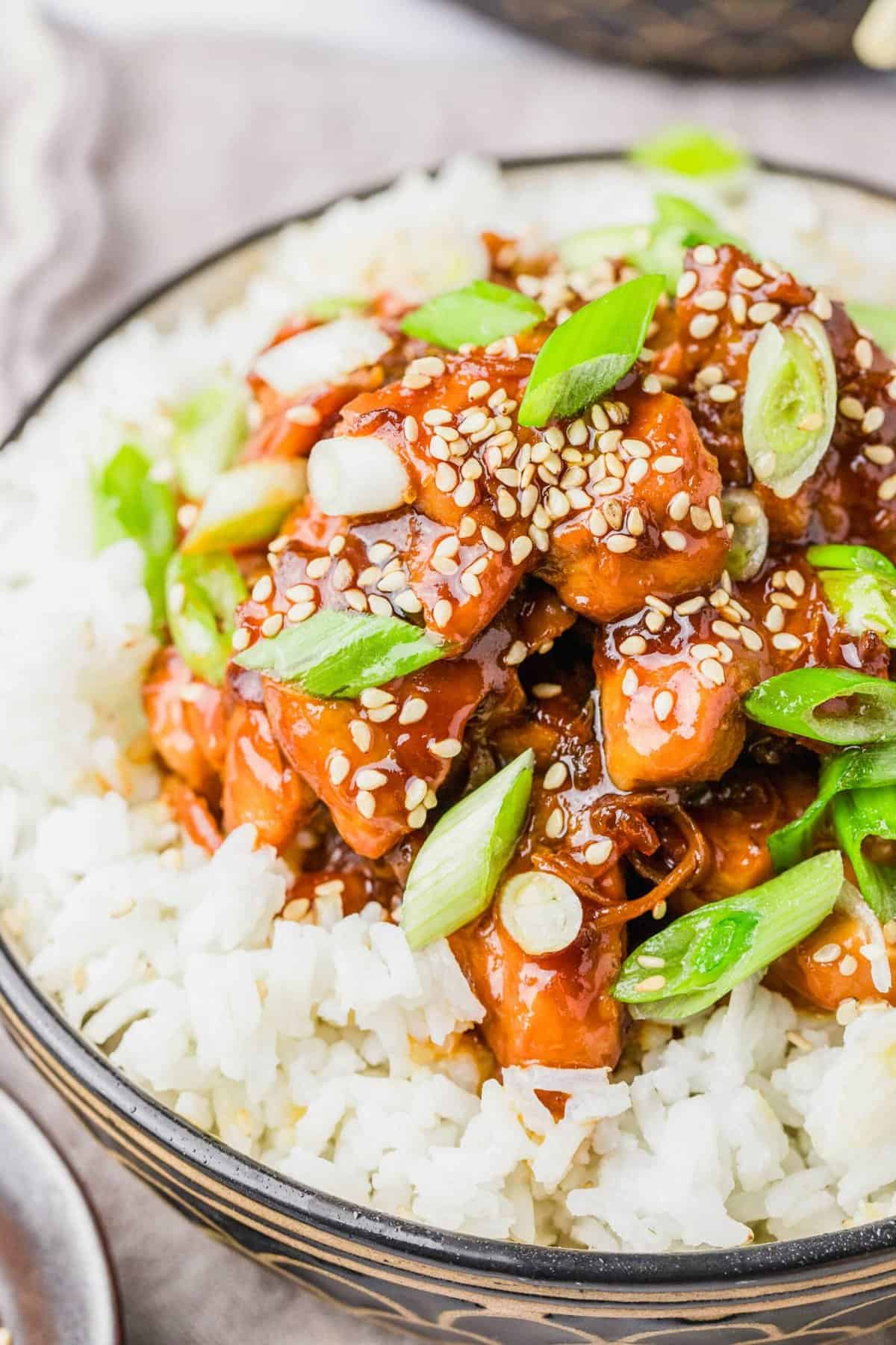 Closeup of honey sesame chicken served over bed of white rice