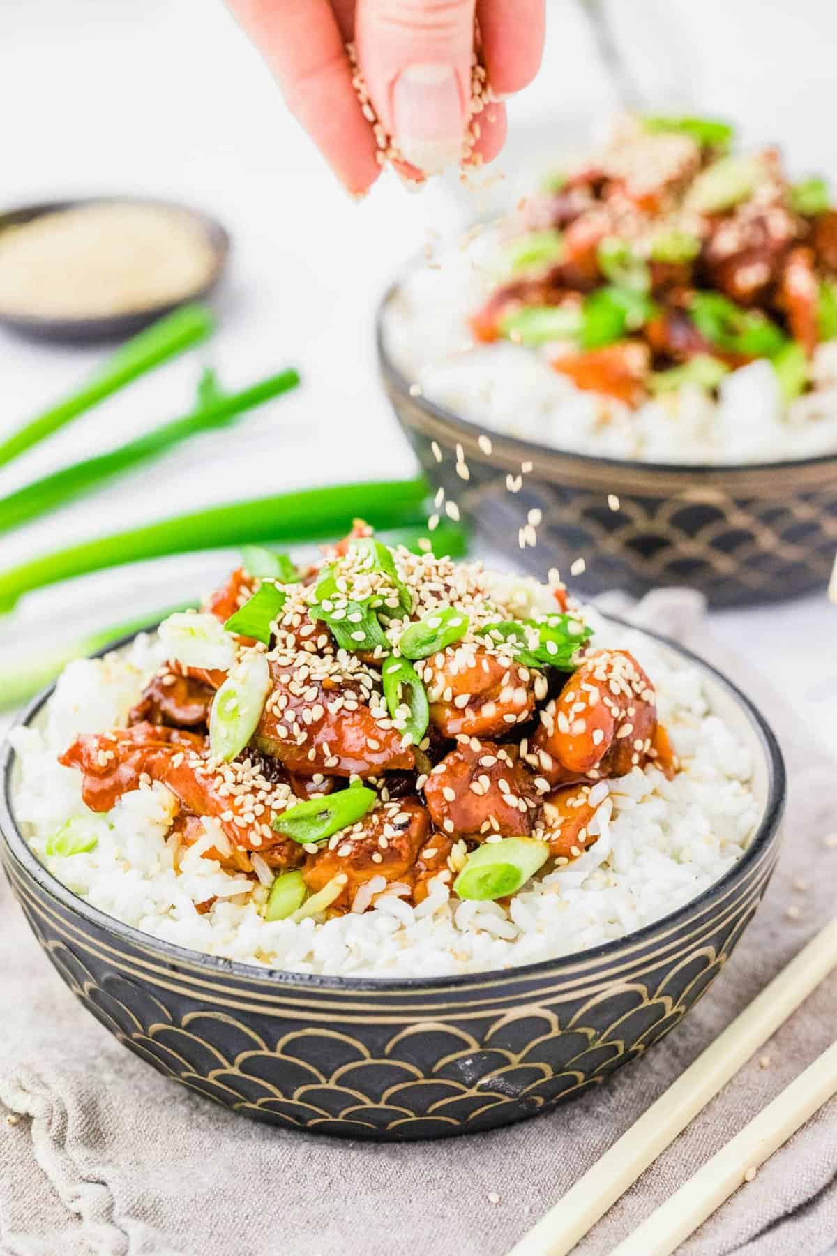 Sprinkling sesame seeds onto bowl of crockpot honey sesame chicken and rice