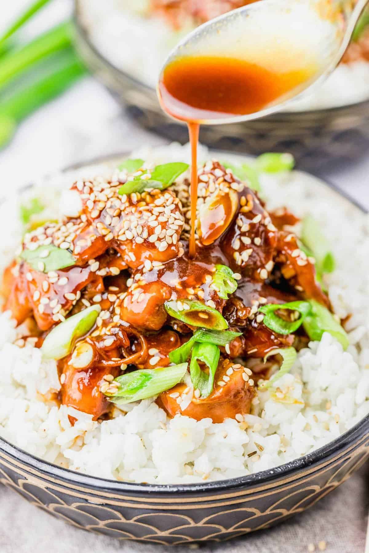 Spoon drizzling sauce onto bowl of rice with honey sesame chicken