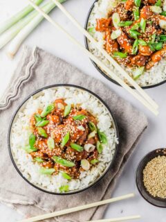 Two bowls of crockpot honey sesame chicken served over white rice, garnished with green onions