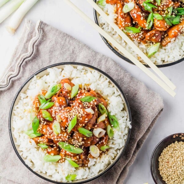 Two bowls of crockpot honey sesame chicken served over white rice, garnished with green onions