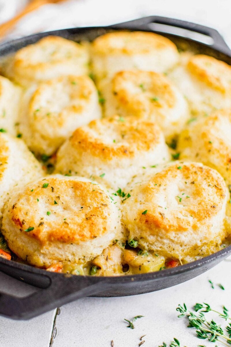 Baked biscuits on top of pot pie in a skillet are garnished with fresh herbs.