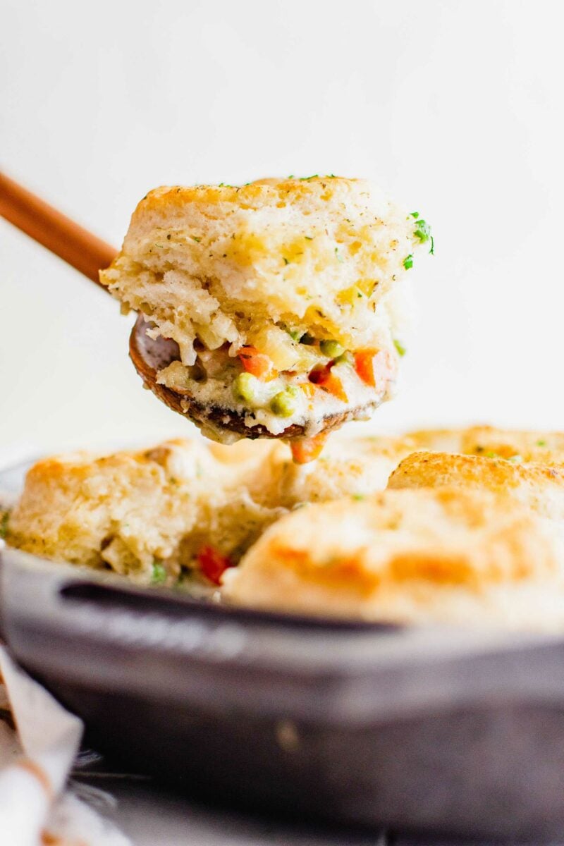 A spoon is lifting a biscuit and pot pie from the skillet.