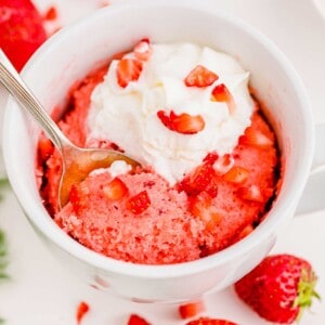 Spoon digging into strawberry mug cake topped with whipped cream