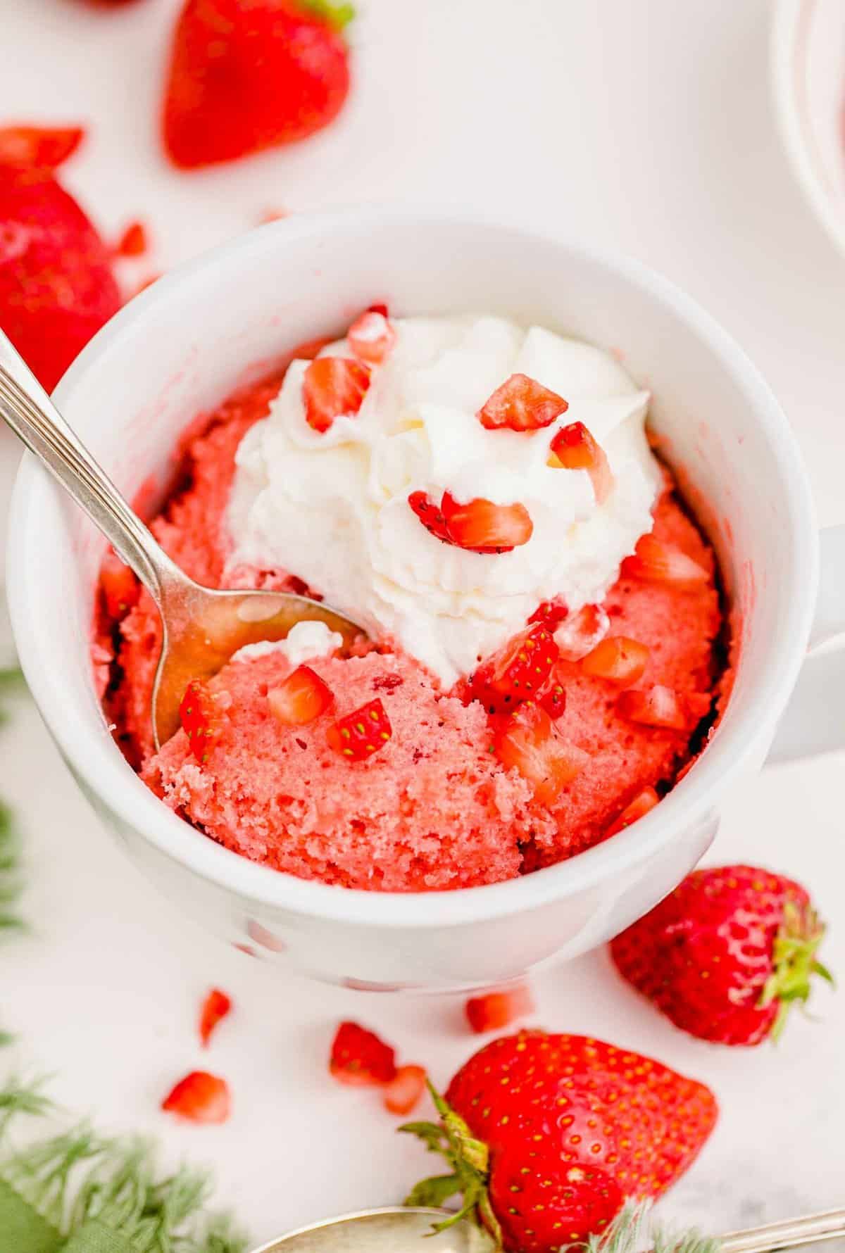 Spoon digging into strawberry mug cake topped with whipped cream