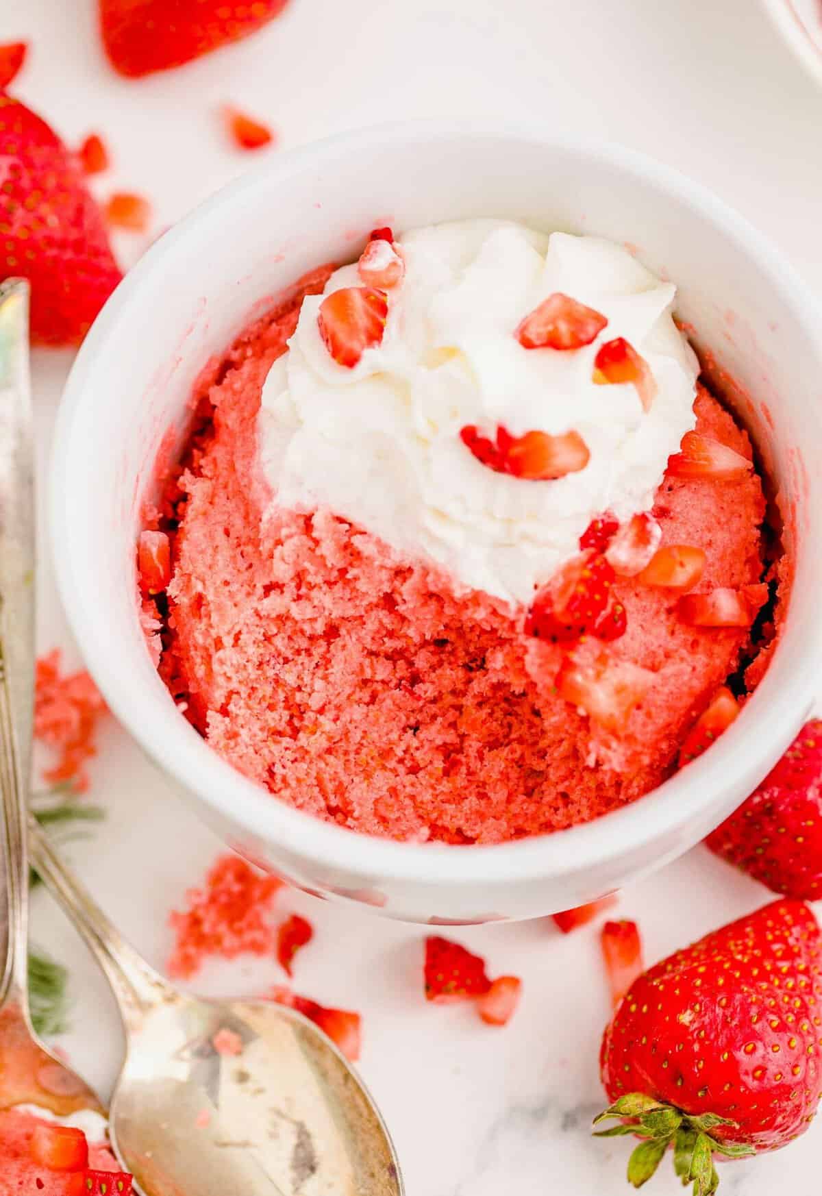 Strawberry cake in mug topped with whipped cream and diced strawberries