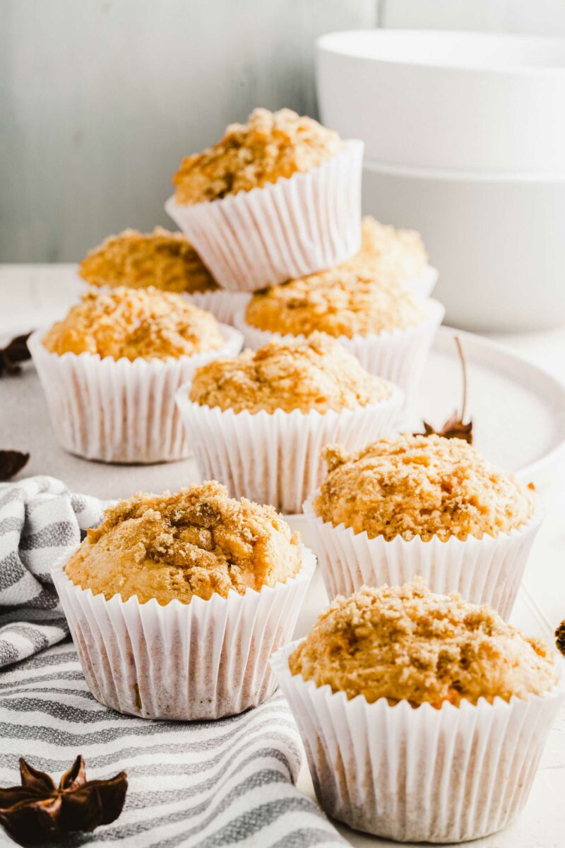 Multiple sweet potato muffins are presented in white cupcake wrappers on a black and white striped tea cloth.