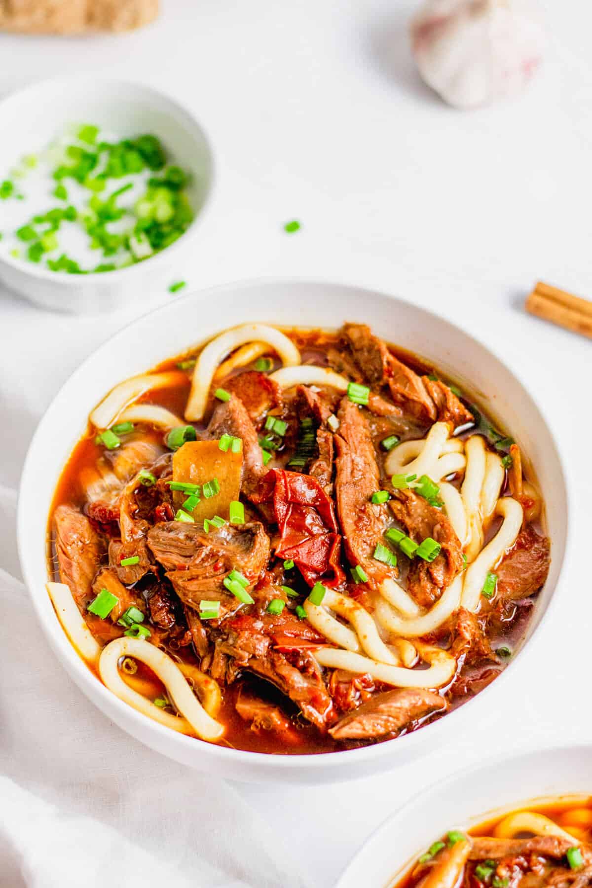 Beef Noodle Soup in white bowl, topped with sliced green onions