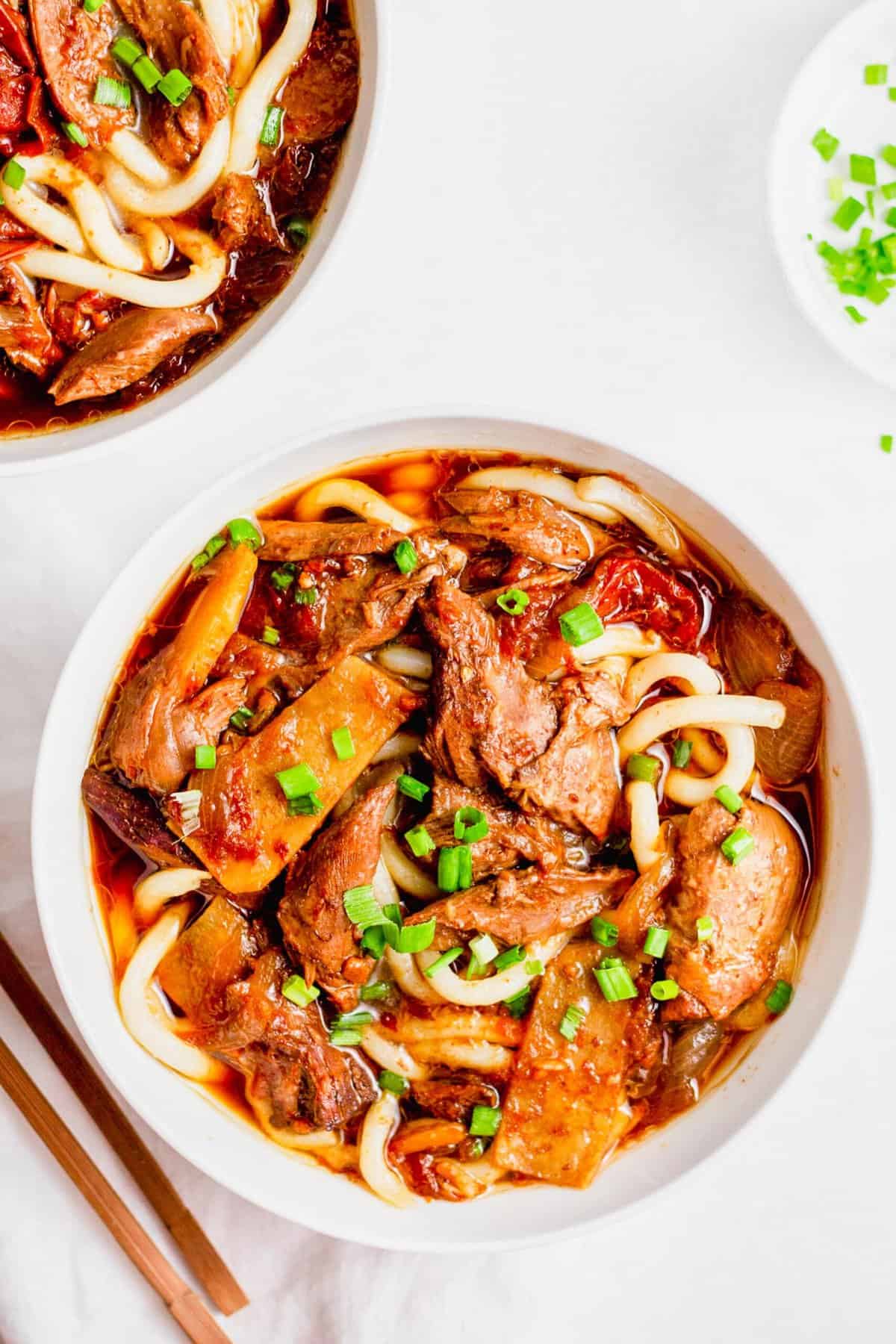 Overhead view of two bowls of Taiwanese beef noodle soup topped with green onions